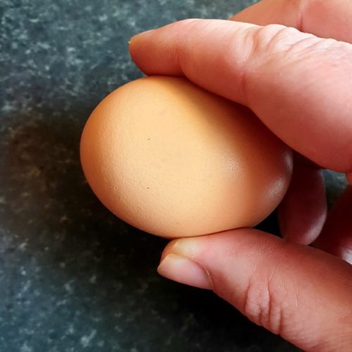 Egg being held between fingers on a worktop surface about to be cracked. 
