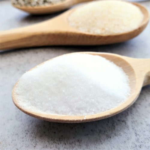 Close up of table salt on a wooden spoon with other spoons of salt blurred in the background.