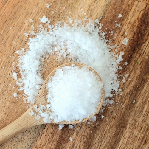 Sea salt flakes spilling off a wooden spoon on a wooden board.
