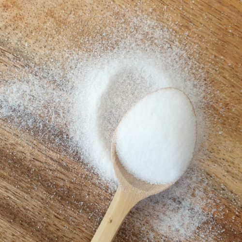 Overhead shot of table salt spilling out of wooden spoon onto a board. 
