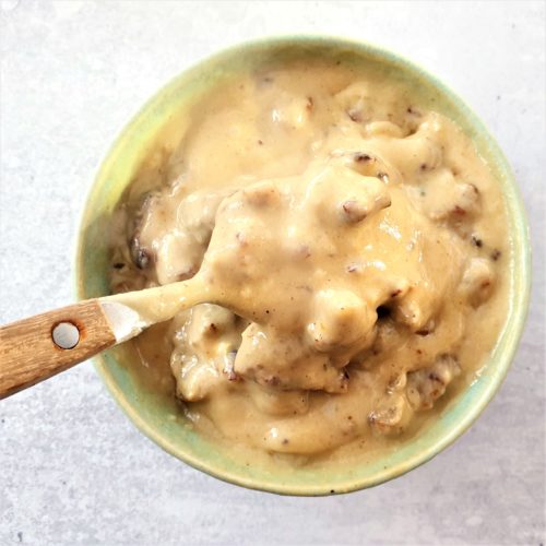 Gravy in a small bowl with a spoon lifting some of the gravy up. 