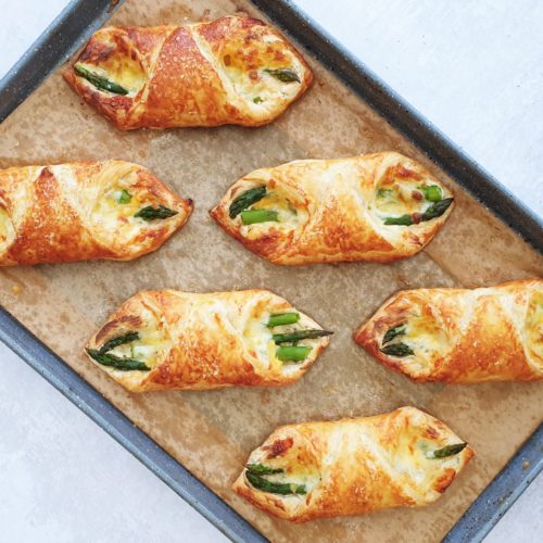 Tray of fresh from the oven puff pastry asparagus wraps shown from overhead at a diagonal angle